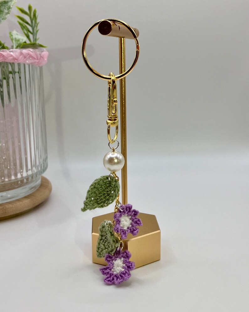 May include: A crocheted flower and leaf keychain with a pearl charm and a gold metal clasp.