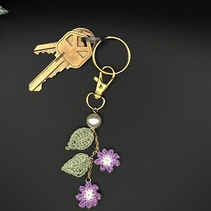 May include: A crocheted flower and leaf keychain with a pearl bead and gold-tone key ring. The keychain is attached to a set of keys.