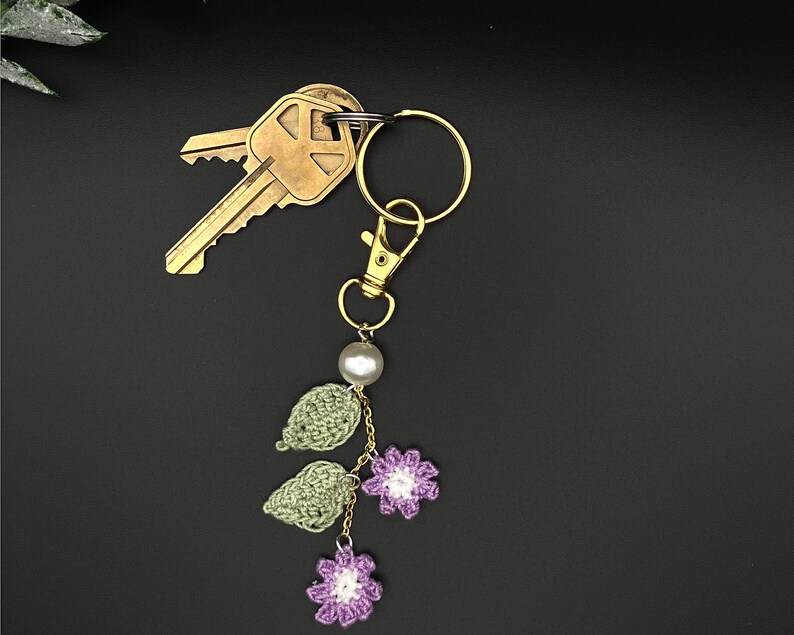 May include: A crocheted flower and leaf keychain with a pearl bead and gold-tone key ring. The keychain is attached to a set of keys.