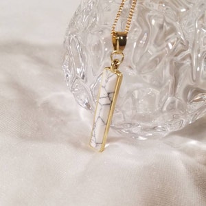 May include: A gold chain necklace with a white marble bar pendant.
