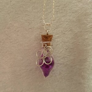 May include: A silver chain necklace with a small glass bottle pendant filled with purple glitter. The bottle is wrapped with silver wire and has a cork stopper.