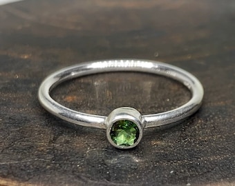 May include: A silver ring with a small, round, green gemstone set in the center.