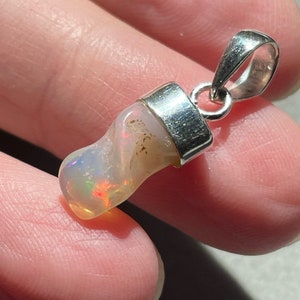 May include: A silver pendant with a white opal stone. The opal has a rainbow iridescent sheen.