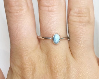 May include: A silver ring with a light blue oval gemstone. The ring is on a person's finger.