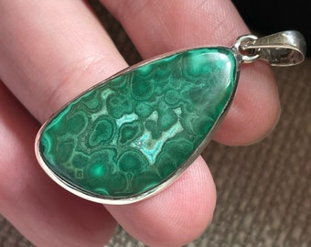 May include: A silver pendant with a green malachite stone. The stone has a swirling pattern of green and white.