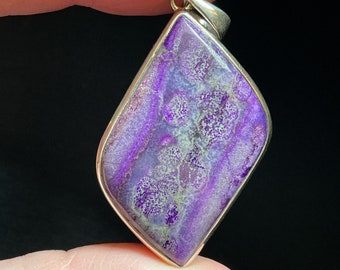 May include: A purple and white gemstone pendant with a silver setting. The pendant is shaped like a diamond and has a unique, swirling pattern.