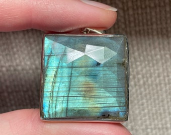 May include: A silver pendant featuring a rectangular, faceted labradorite gemstone with iridescent blue, green, and gold hues.
