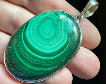 May include: A green malachite pendant with a silver bail. The malachite has a swirling pattern of green and black.