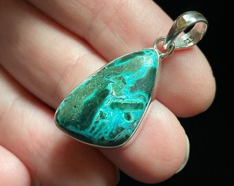 May include: A silver pendant featuring a green and black malachite gemstone. The pendant is in the shape of a teardrop and has a silver bail.