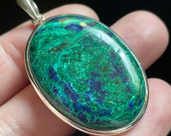 May include: A silver pendant featuring a large oval-shaped green and blue gemstone. The gemstone has a swirling pattern of green and blue.
