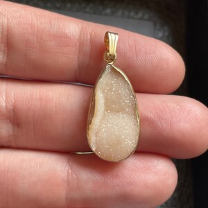 Puede incluir: Un colgante de oro con un cristal de cuarzo transparente en forma de l&aacute;grima, con un interior brillante, blanco y transl&uacute;cido.