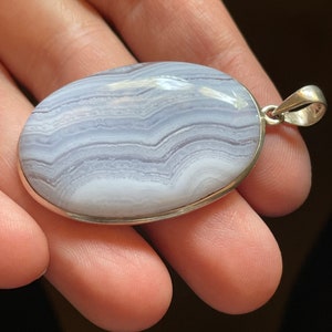 Könnte beinhalten: Ein silberner Anhänger mit einem hellblauen und weißen Achat-Stein mit einem wirbelnden Muster. Der Stein ist oval geformt und in einer silbernen Fassung gefasst.