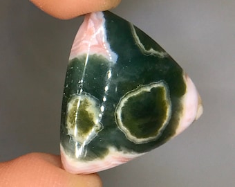 Op de afbeelding: Een driehoekige, gepolijste edelsteen met een glad oppervlak en een opvallend kleurpatroon van diep bosgroen en zacht pastelroze. De steen vertoont natuurlijke cirkelvormige insluitingen met witte randen, wat zorgt voor een contrast tussen de groene en roze minerale lagen.