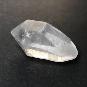 Könnte beinhalten: Ein klarer Quarzkristall mit einer spitzen Spitze und einer glatten, polierten Oberfläche.