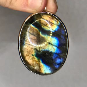 May include: A silver oval pendant with a large iridescent labradorite gemstone. The stone has a blue, green, and gold color.