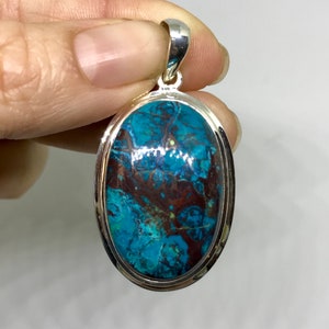 Peut inclure: Un pendentif en argent avec une grande pierre turquoise de forme ovale. La pierre pr&eacute;sente un motif tourbillonnant de bleu, de vert et de brun.