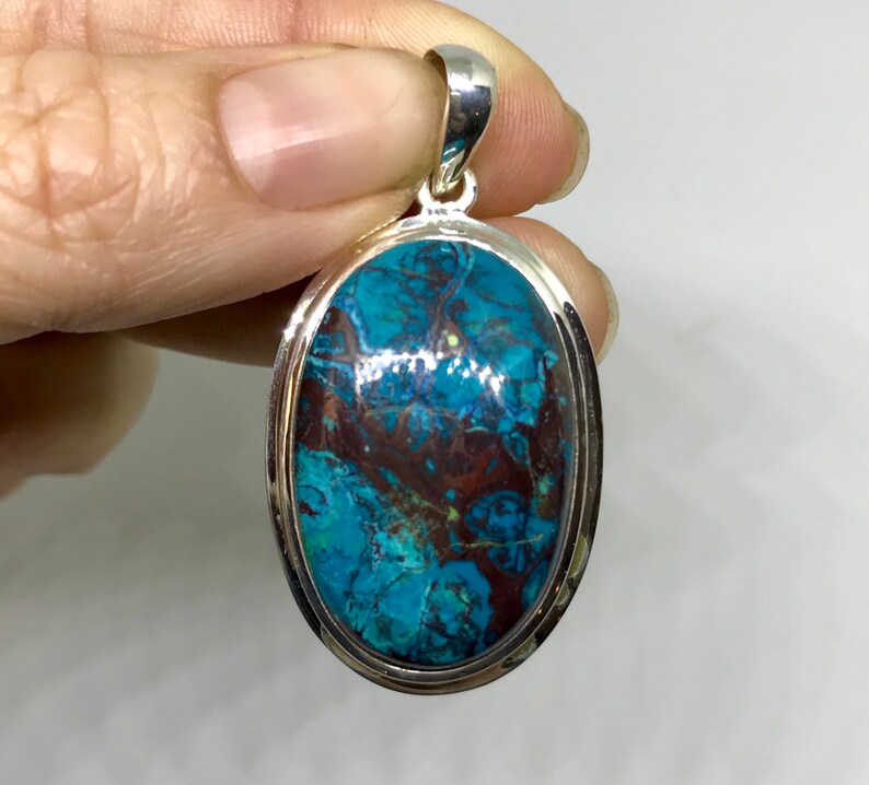 Peut inclure: Un pendentif en argent avec une grande pierre turquoise de forme ovale. La pierre pr&eacute;sente un motif tourbillonnant de bleu, de vert et de brun.