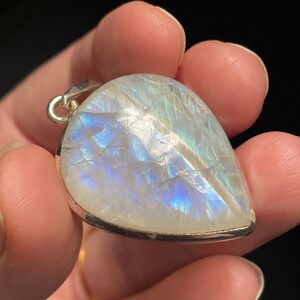 May include: A teardrop-shaped moonstone pendant with a silver setting. The moonstone has a milky white color with iridescent blue and white flashes.