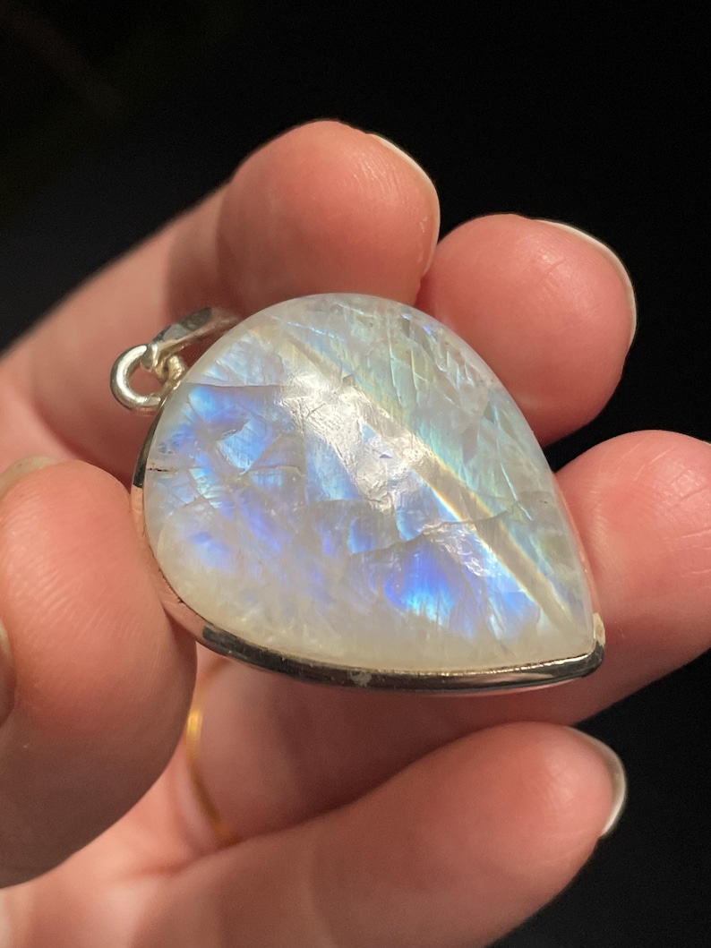May include: A teardrop-shaped moonstone pendant with a silver setting. The moonstone has a milky white color with iridescent blue and white flashes.