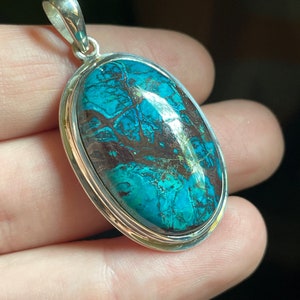 Peut inclure: Un pendentif en argent avec une grande pierre ovale turquoise. La pierre pr&eacute;sente un motif tourbillonnant de bleu, de vert et de brun.