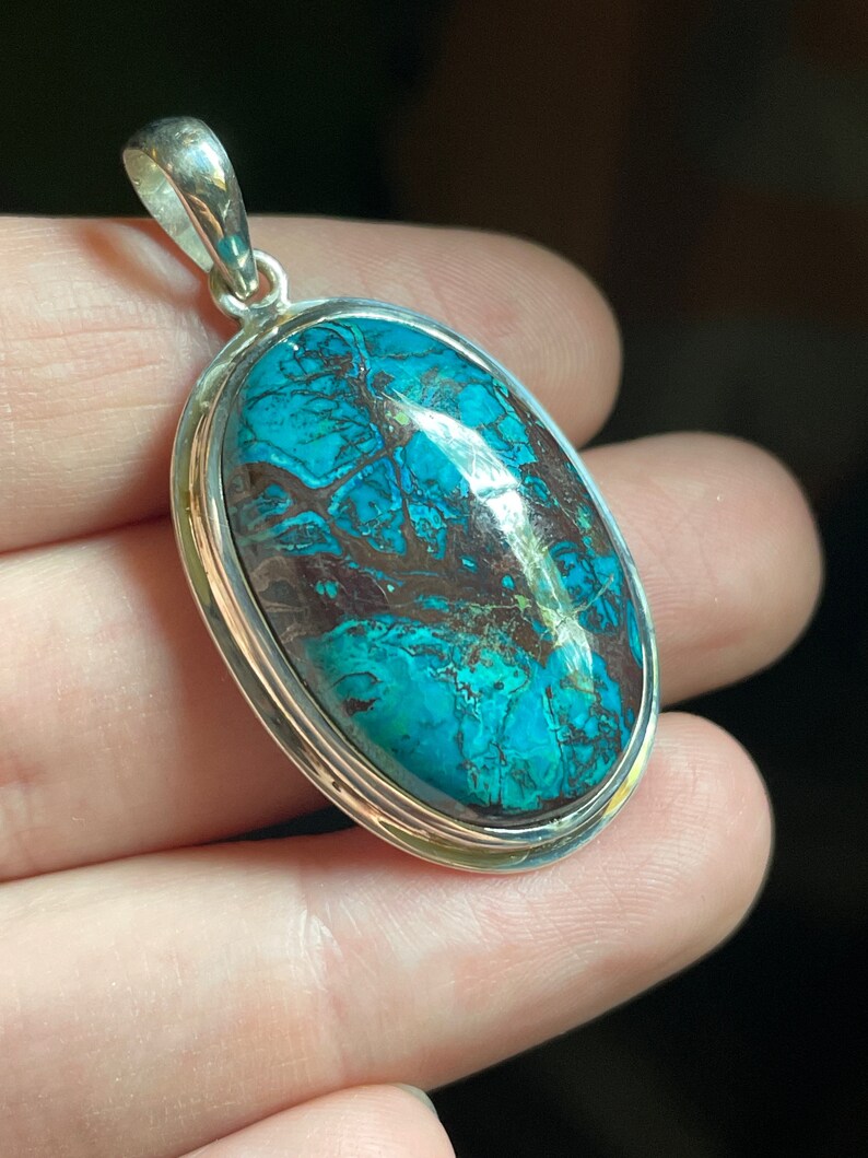 Peut inclure: Un pendentif en argent avec une grande pierre ovale turquoise. La pierre pr&eacute;sente un motif tourbillonnant de bleu, de vert et de brun.