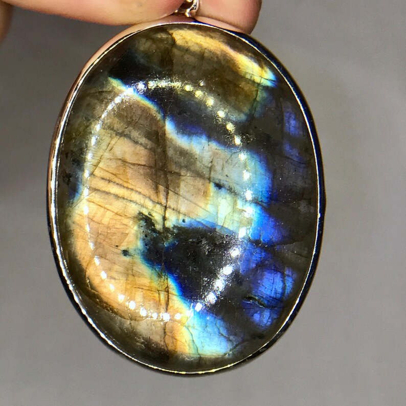 May include: Oval-shaped labradorite pendant with a silver setting. The stone has a blue, green, and gold iridescent sheen.