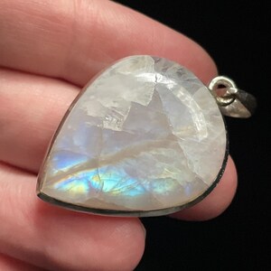May include: A teardrop-shaped moonstone pendant with a silver setting. The moonstone has a milky white color with iridescent blue and green flashes.