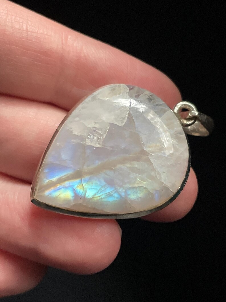 May include: A teardrop-shaped moonstone pendant with a silver setting. The moonstone has a milky white color with iridescent blue and green flashes.