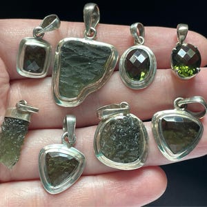 Puede incluir: Una colecci&oacute;n de ocho colgantes de plata con detalles de piedras preciosas verdes. Los colgantes presentan diversas formas y tama&ntilde;os, incluyendo una l&aacute;grima, un tri&aacute;ngulo, un c&iacute;rculo y un rect&aacute;ngulo. Las piedras preciosas son de varios tonos de verde, desde claro hasta oscuro.