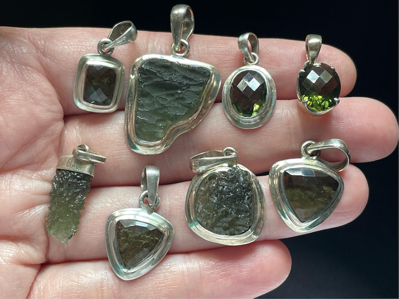 Puede incluir: Una colecci&oacute;n de ocho colgantes de plata con detalles de piedras preciosas verdes. Los colgantes presentan diversas formas y tama&ntilde;os, incluyendo una l&aacute;grima, un tri&aacute;ngulo, un c&iacute;rculo y un rect&aacute;ngulo. Las piedras preciosas son de varios tonos de verde, desde claro hasta oscuro.