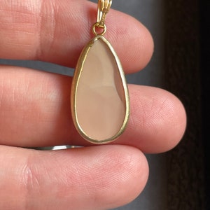 Puede incluir: Un colgante en forma de l&aacute;grima con una piedra rosa claro engastada en un marco de oro.