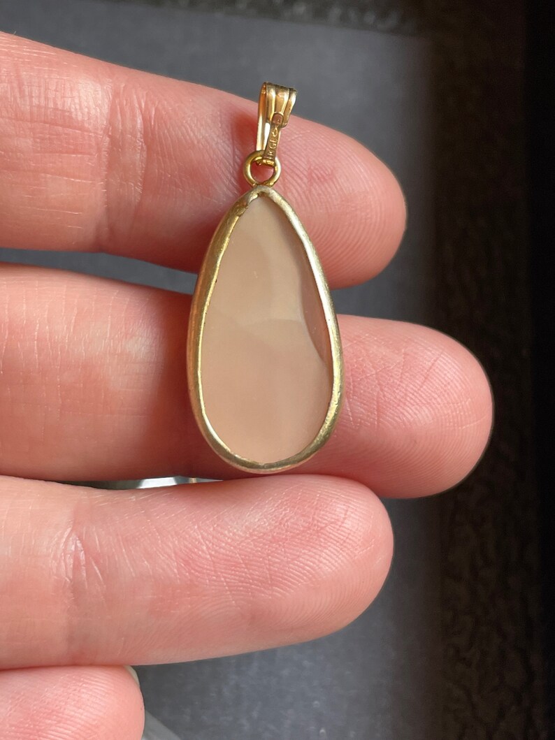 Puede incluir: Un colgante en forma de l&aacute;grima con una piedra rosa claro engastada en un marco de oro.