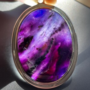 May include: A silver pendant with a purple and white agate stone. The stone has a swirling pattern and is set in a silver oval frame.