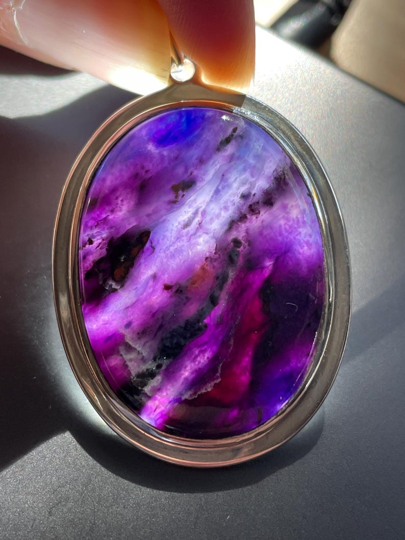 May include: A silver pendant with a purple and white agate stone. The stone has a swirling pattern and is set in a silver oval frame.