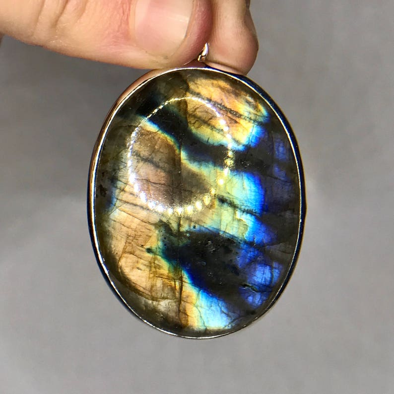 May include: A silver oval pendant with a large iridescent labradorite gemstone. The stone has a blue, green, and gold color.