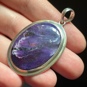 May include: A silver pendant with a purple and white stone set in a silver oval frame. The pendant has a silver bail with the number "925" stamped on it.