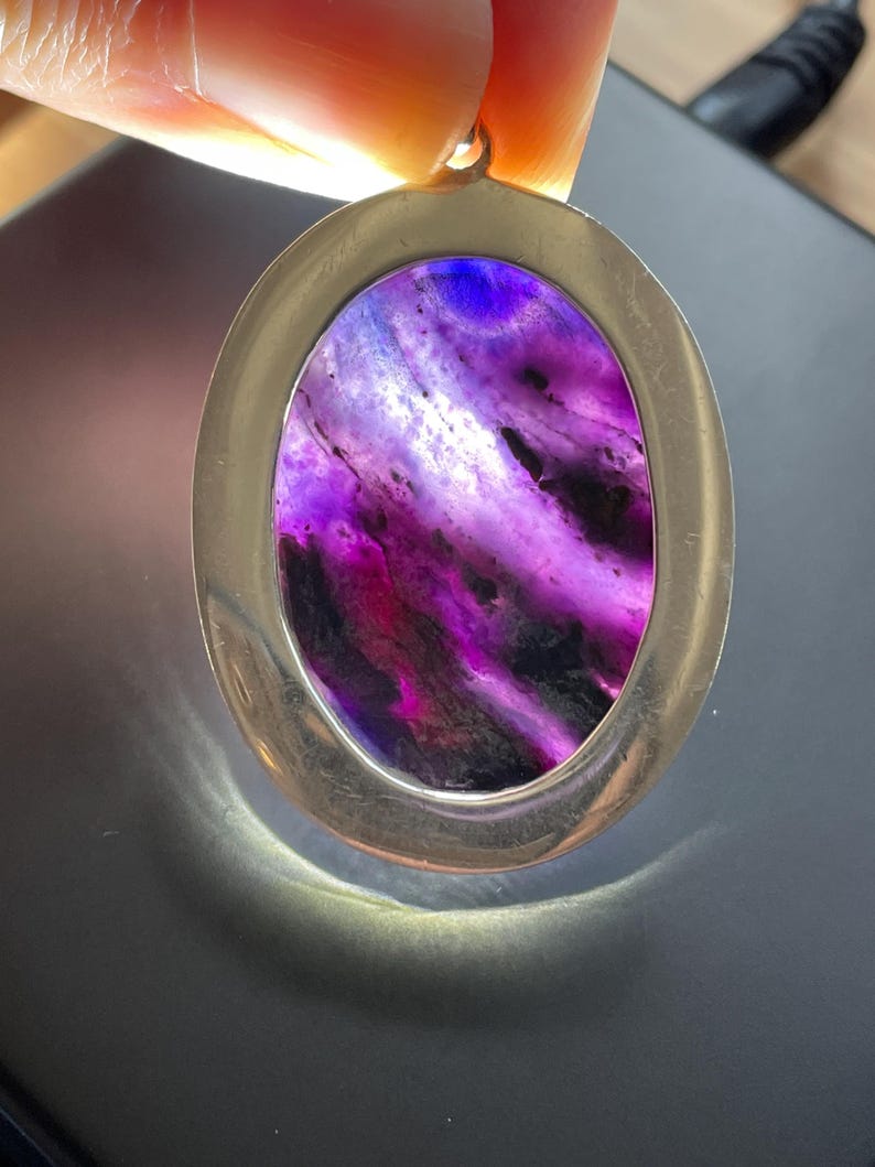 May include: A silver oval pendant with a purple and white agate stone. The stone has a swirling pattern and is set in a silver frame.