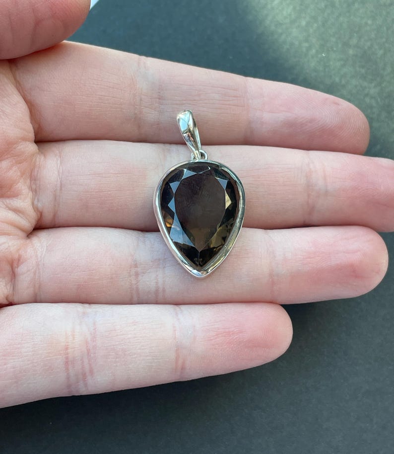 May include: A silver pendant with a teardrop-shaped smoky quartz gemstone.