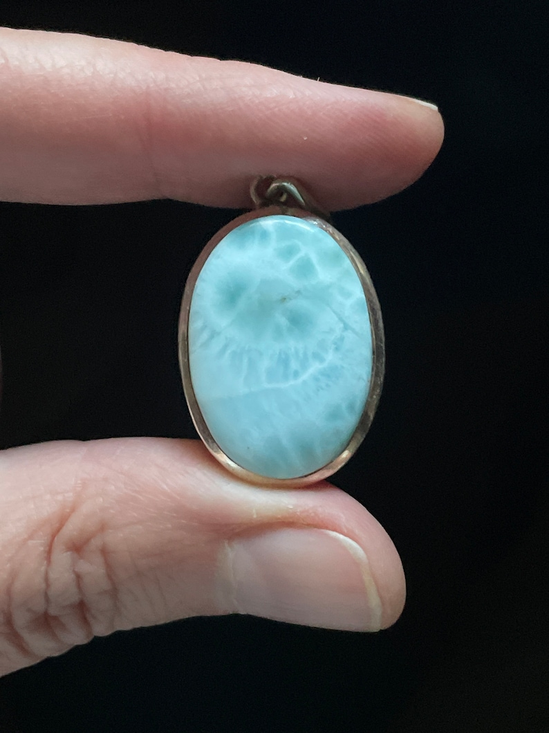 Puede incluir: Pendiente de forma ovalada con una piedra preciosa azul claro y blanca engastada en un marco de metal plateado.