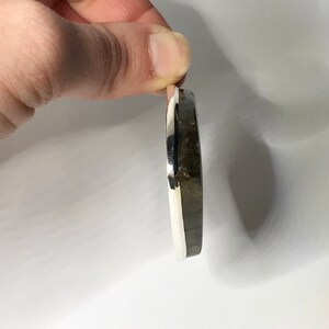 K&ouml;nnte beinhalten: Ein silberner Ring mit einem dunkelgrauen Stein, der in der Mitte eingesetzt ist. Der Ring wird von der Seite gezeigt, wobei der Stein zum Betrachter zeigt.