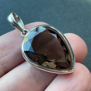 May include: A teardrop-shaped smoky quartz pendant set in sterling silver. The pendant is faceted and has a dark brown color.