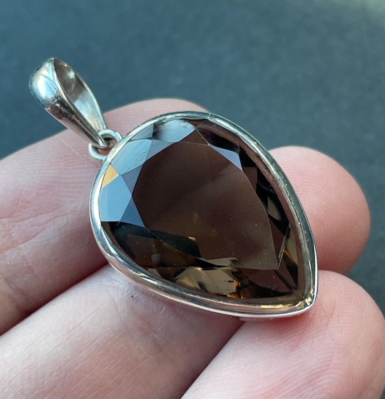 May include: A teardrop-shaped smoky quartz pendant set in sterling silver. The pendant is faceted and has a dark brown color.