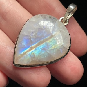 May include: A teardrop-shaped moonstone pendant with a silver setting. The moonstone has a rainbow sheen and is set in a silver bezel.