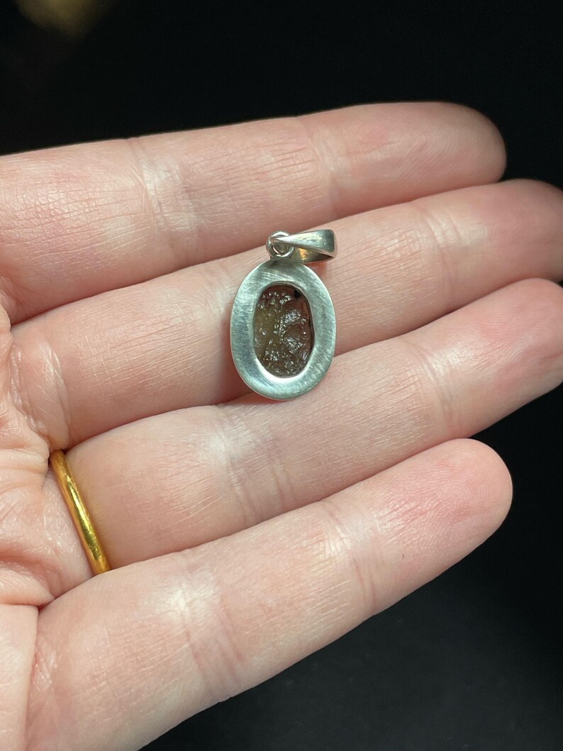 Puede incluir: Pendiente de plata con un engaste ovalado que presenta una piedra transparente y facetada de color marr&oacute;n.