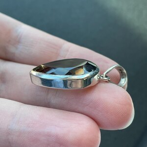 May include: A silver pendant with a dark brown pear-shaped gemstone.
