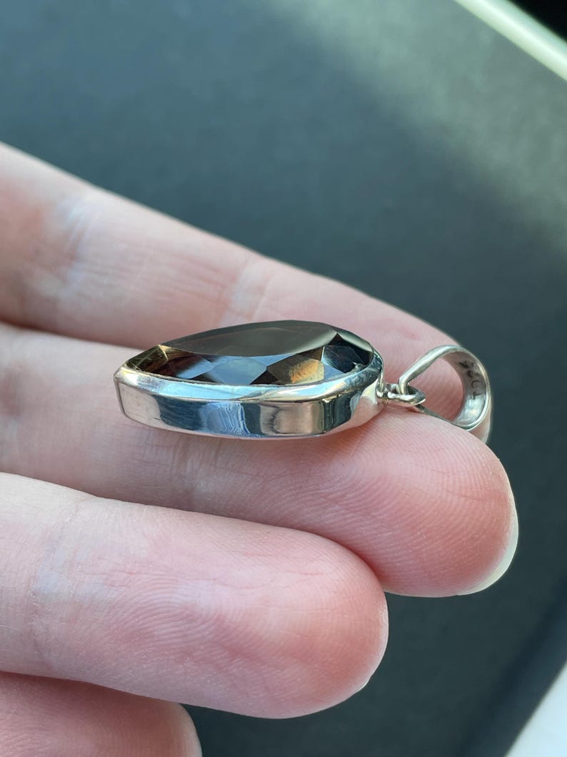 May include: A silver pendant with a dark brown pear-shaped gemstone.