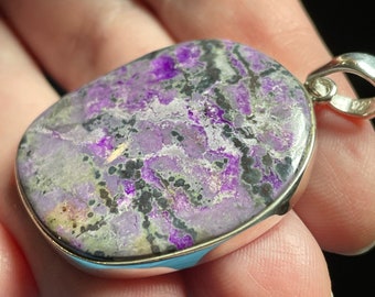May include: A silver pendant with a purple and black stone. The stone has a swirling pattern and is set in a silver bezel.