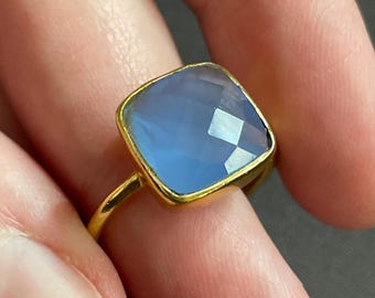 May include: A gold ring with a light blue square-shaped gemstone.