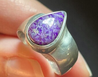May include: A silver ring featuring a teardrop-shaped purple and white gemstone.
