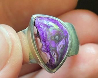 May include: A silver ring with a purple and white gemstone set in a triangular shape.